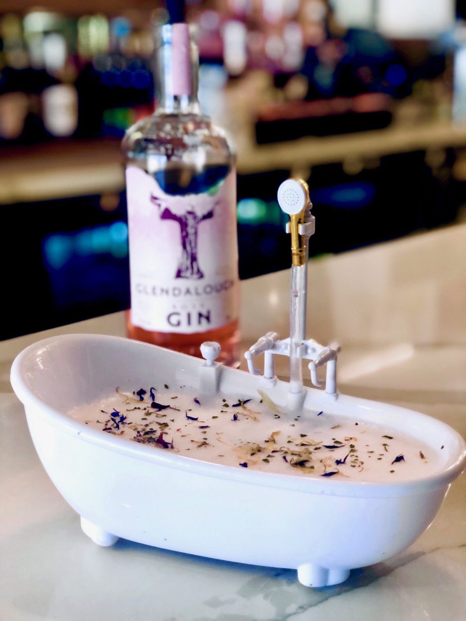 A Rose Gin cocktail served in a Bathtub vessel with edible flowers.